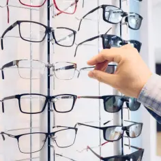 Ręka wybiera okulary z apteki. Wiele oprawek w różnych stylach i kolorach czeka na klientów.