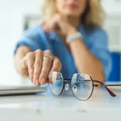 Kobieta w niebieskiej bluzce podaje okulary plusy do chodzenia.