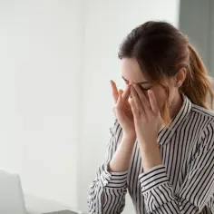 Kobieta z zapaleniem spojówek masuje oczy, zmęczona pracą przy komputerze.