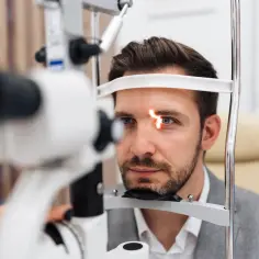 Badanie wzroku mężczyzny z czerwonym światłem na oku. Może to być kontrola po zabiegu, np. w celu wykrycia powikłania po laserowej korekcji wzroku.