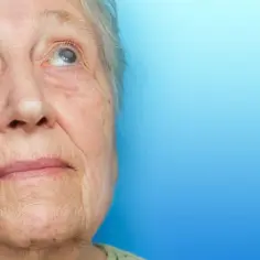 Twarz starszej kobiety z widocznym zmętnieniem soczewki w jednym oku, co może być jednym z objawów zaćmy.