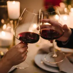 Dwie osoby wznoszą toast kieliszkami czerwonego wina przy świecach. Czy po operacji zaćmy można pić alkohol?