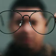 Osoba trzyma nowe okulary, przez które świat wydaje się lekko zakrzywiony.