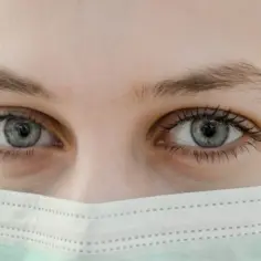 Szare oczy, lekko nieostre widzenie po laserowej korekcji wzroku, pod zieloną maseczką ochronną.