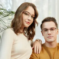 Para stylowych osób w okularach bez oprawek, ona w beżowym swetrze, on w musztardowym.