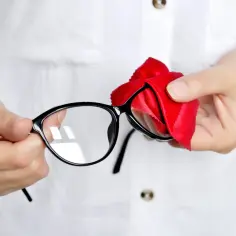 Dłonie czyszczą czarne okulary czerwoną ściereczką z mikrofibry. Dowiedz się, czym czyścić okulary, by były idealnie przejrzyste.
