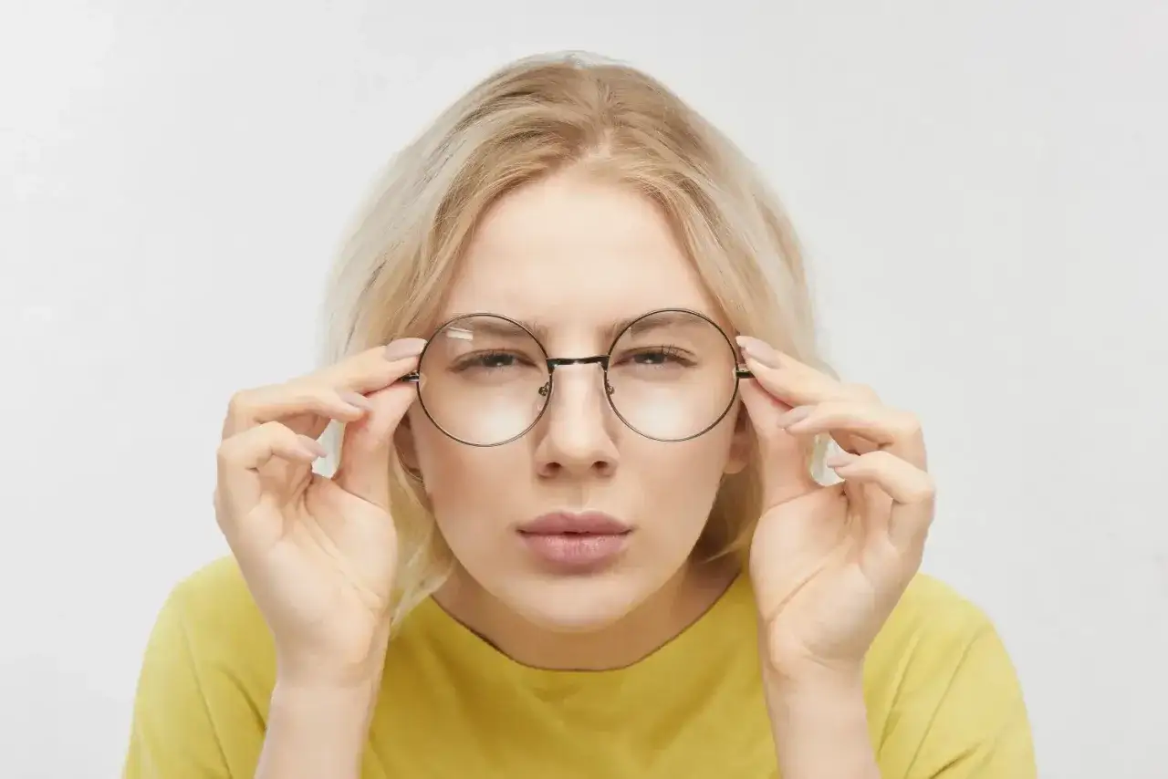 Blondynka z wadą wzroku 5, poprawiająca okrągłe okulary, próbuje skupić wzrok.