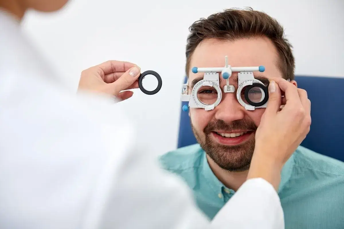 Mężczyzna uśmiecha się, gdy optometrysta testuje jego wzrok za pomocą specjalnych okularów.