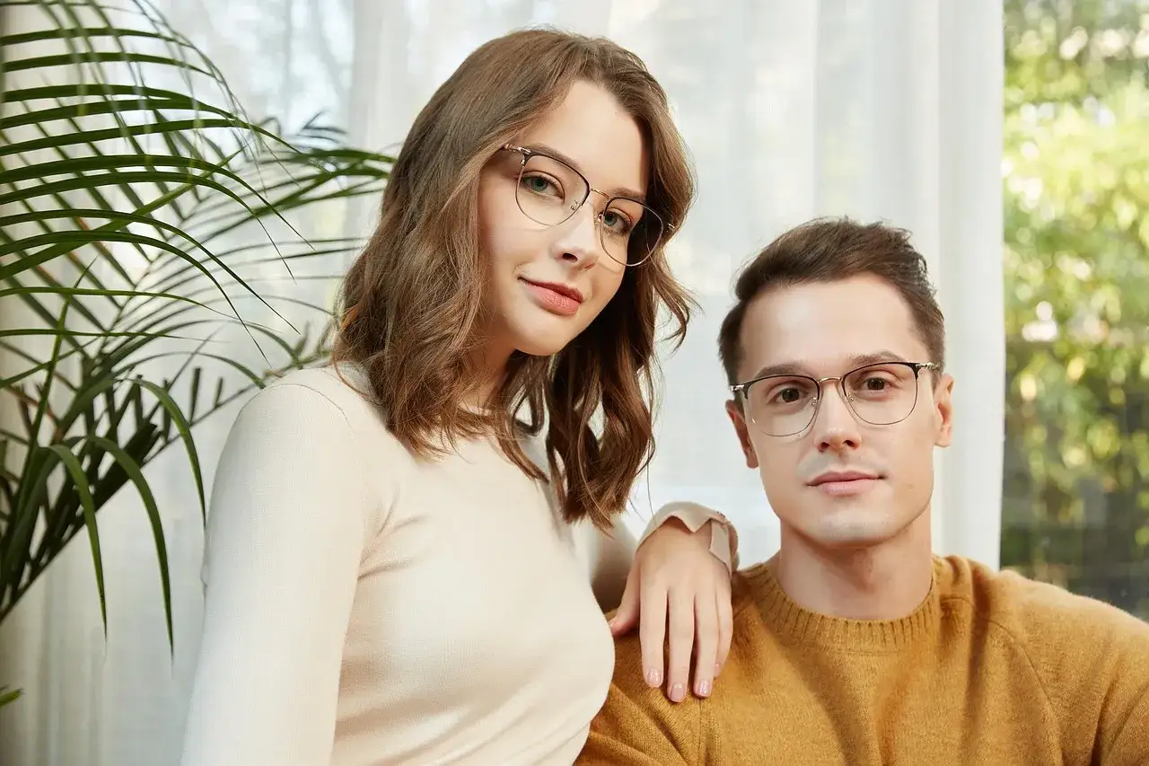 Para stylowych osób w okularach bez oprawek, ona w jasnym swetrze, on w musztardowym.