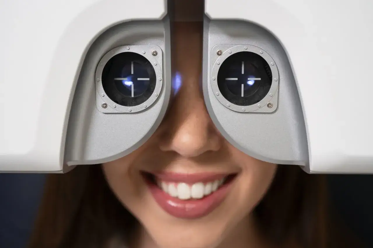 Uśmiechnięta kobieta podczas badania wzroku przed laserową korekcją. Zastanawia się, ile L4 będzie potrzebne po zabiegu.